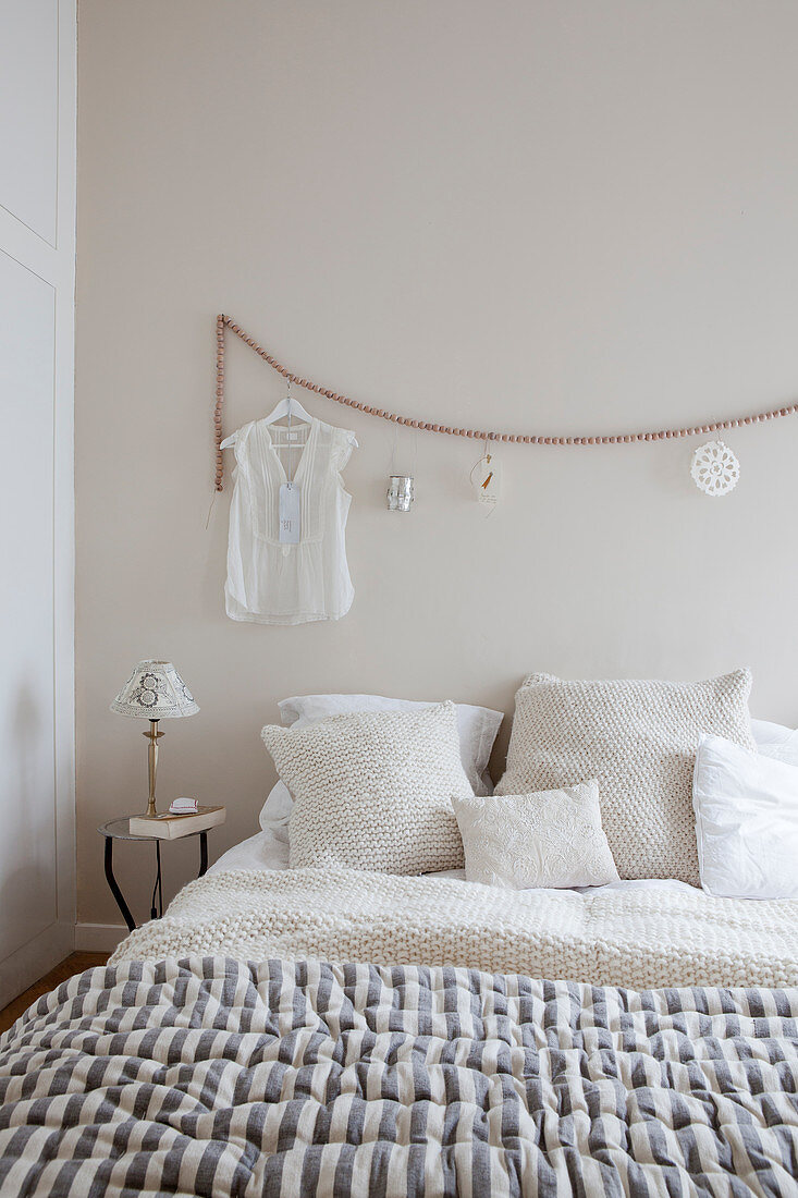 Doppelbett mit Kissen, Damenbluse an Holzperlenkette hängend im Schlafzimmer in Beigetönen