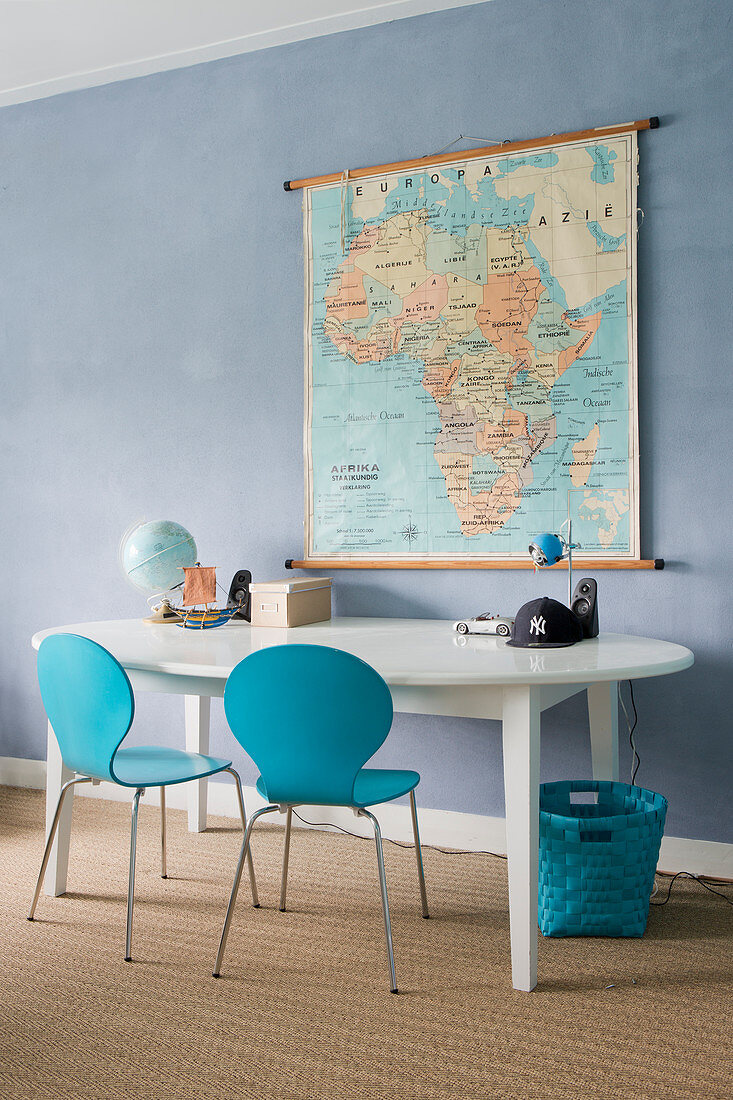 Zwei blaue Stühle an ovalem Tisch vor blauer Wand mit Landkarte