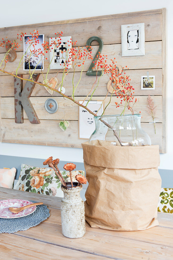 Branch of berries in glass vase in brown paper bag in front of pinboard made from wooden planks