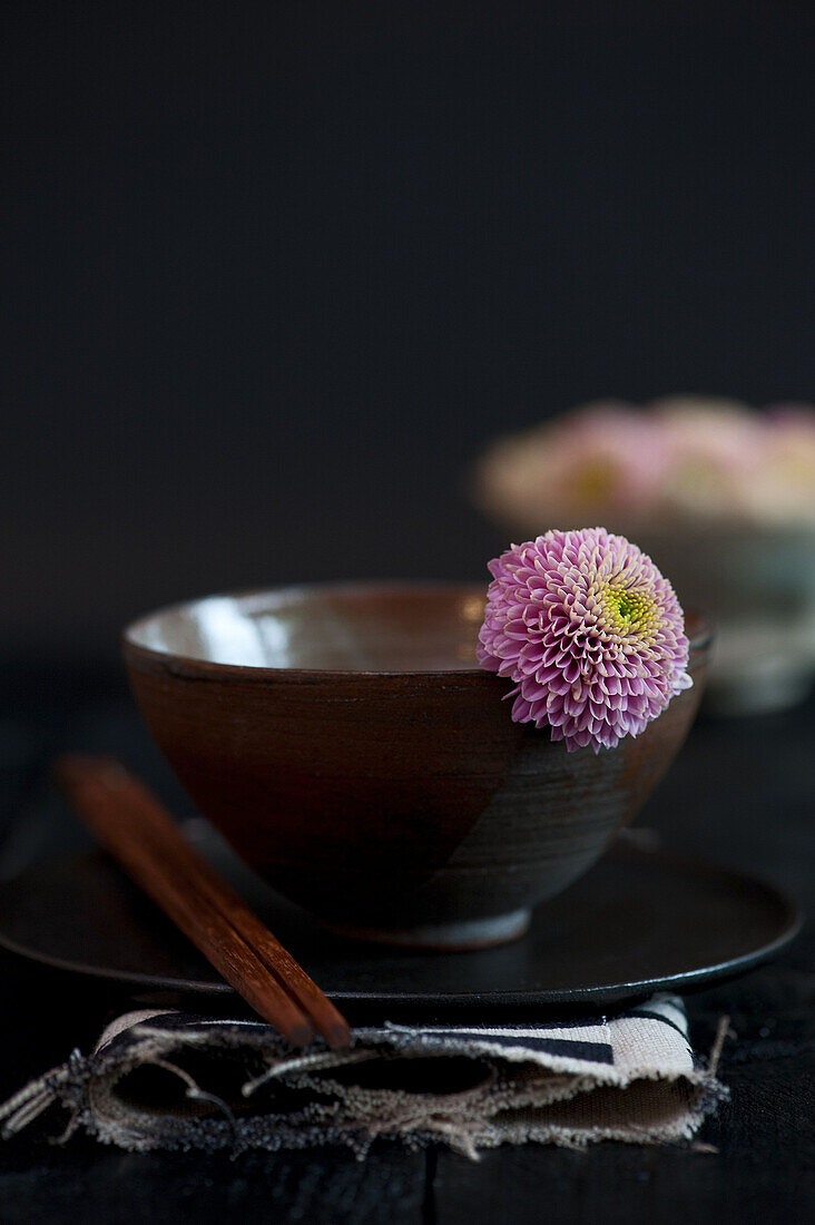 Brown ceramic bowl with wooden sticks and purple chrysanthemum