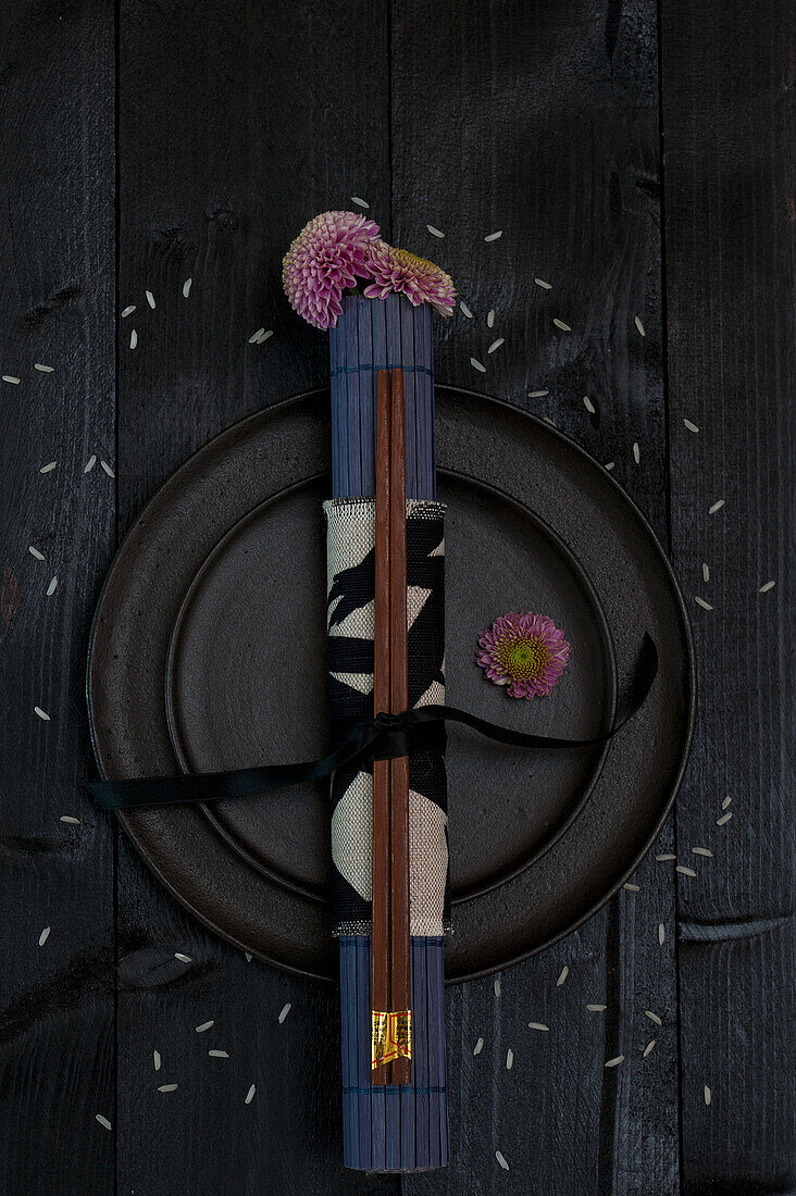 Black plate with chopsticks and flowers on a dark wooden table