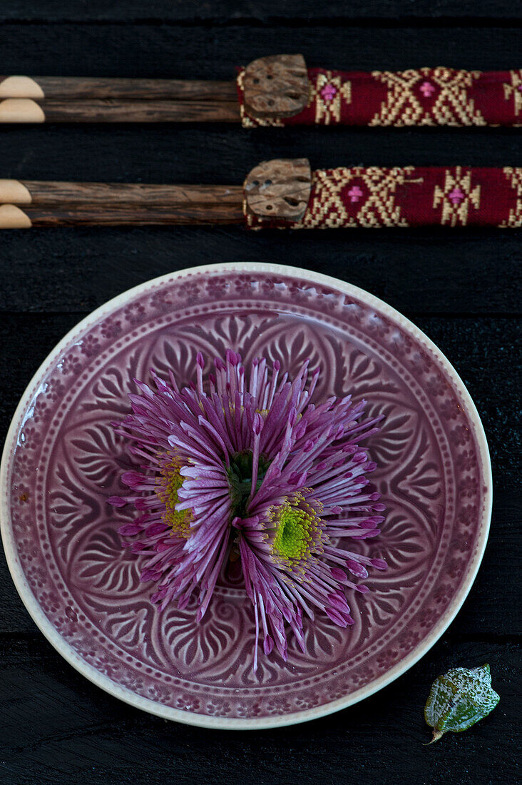 Purple chrysanthemums (Chrysanthemum) on an ornately patterned plate