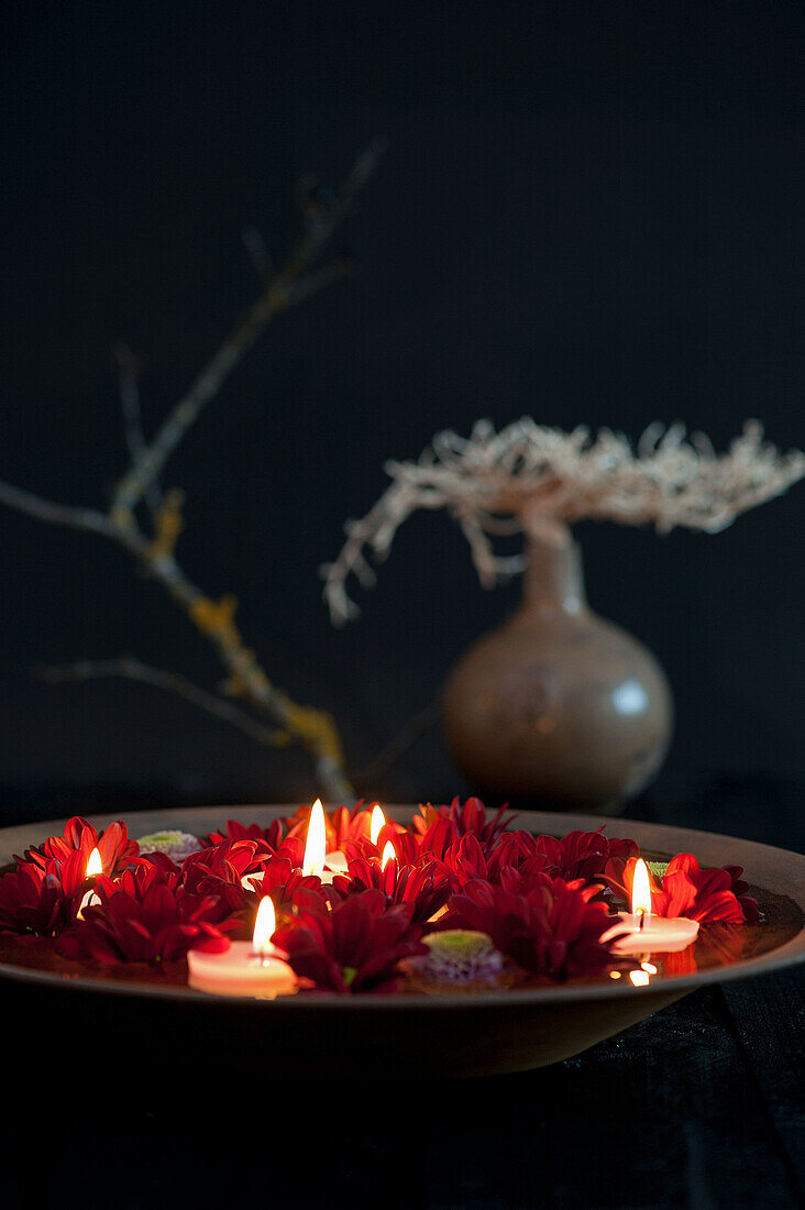 Floating tea lights in a bowl with red flowers against a black background