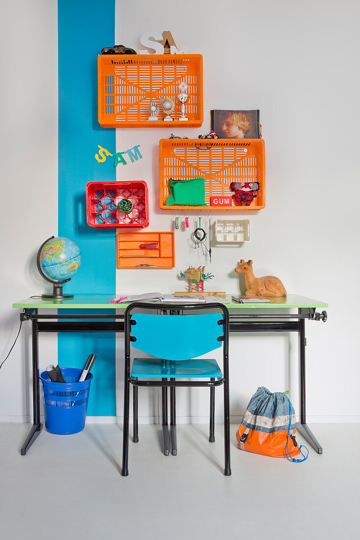 Desk against wall with blue stripe and below colourful plastic crates used as shelf modules