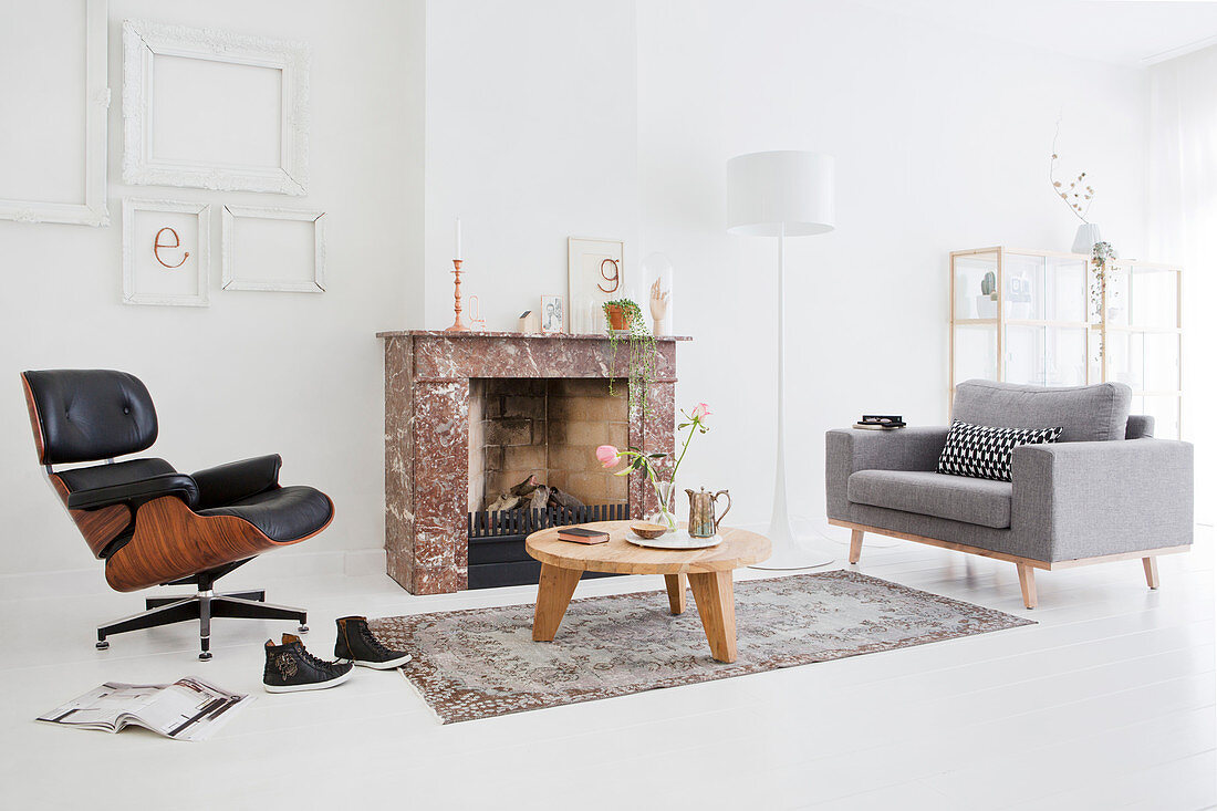 Classic Eames Lounge Chair, coffee table and grey armchair in front of fireplace in white living room