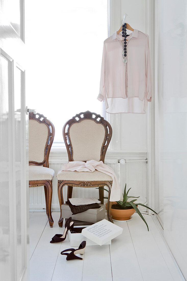 Antique upholstered chairs and ladies' clothing in bright room