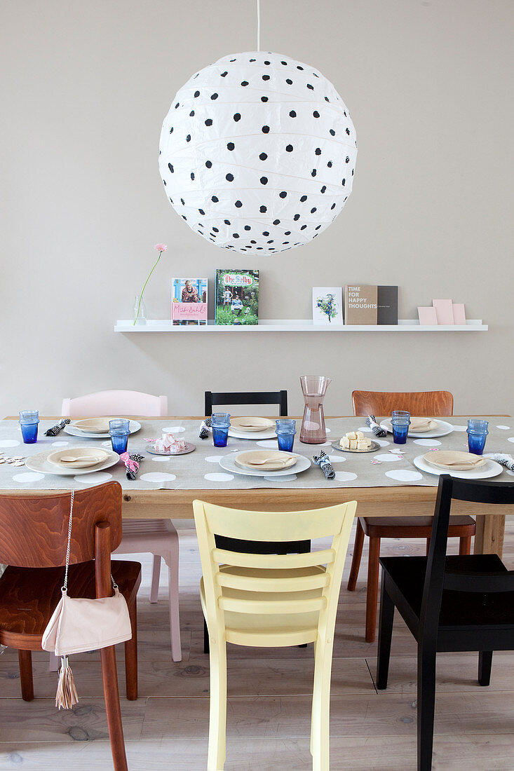Gedeckter Tisch mit verschiedenen Stühlen, darüber schwarz-weiß gepunkteter Papierlampenschirm