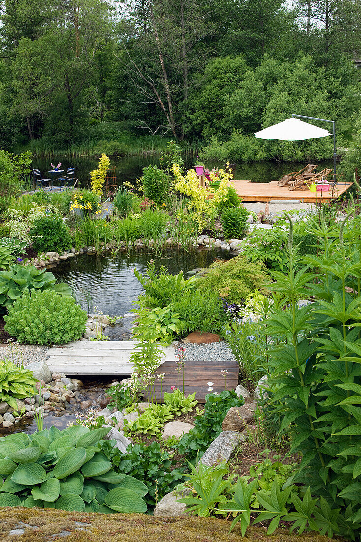 Idyllic garden pond with stone border, wooden walkways, and wooden sun deck