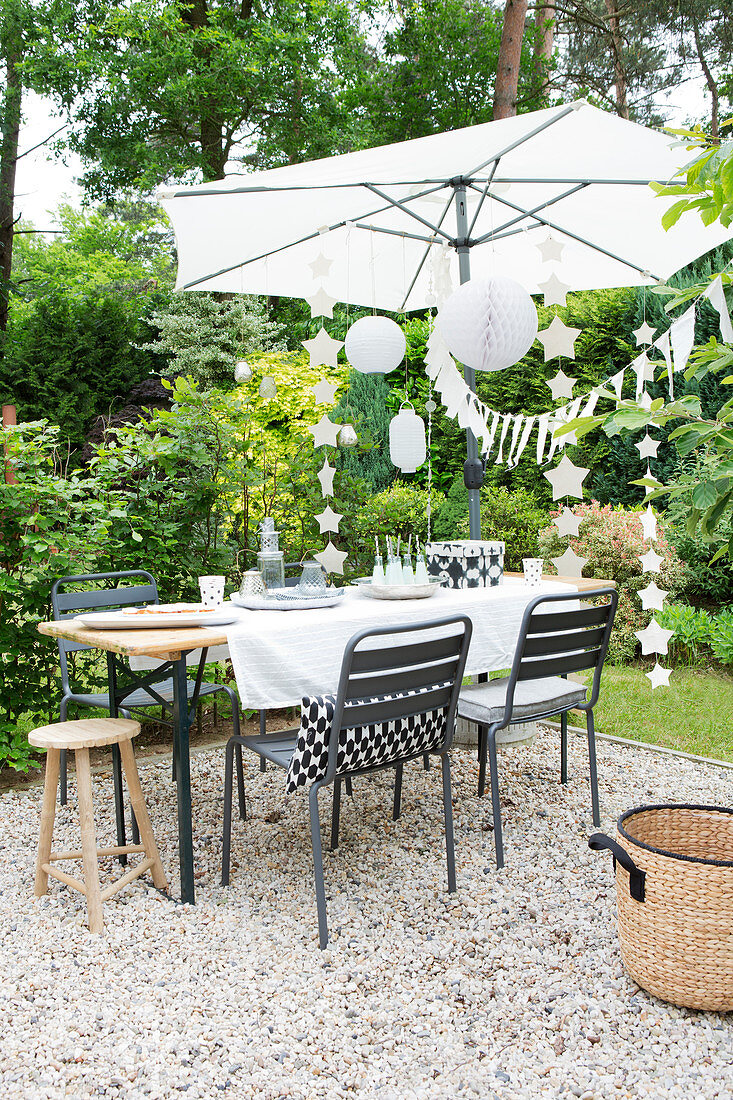 Gedeckter Tisch, Sonnenschirm und Partydeko in sommerlichem Garten