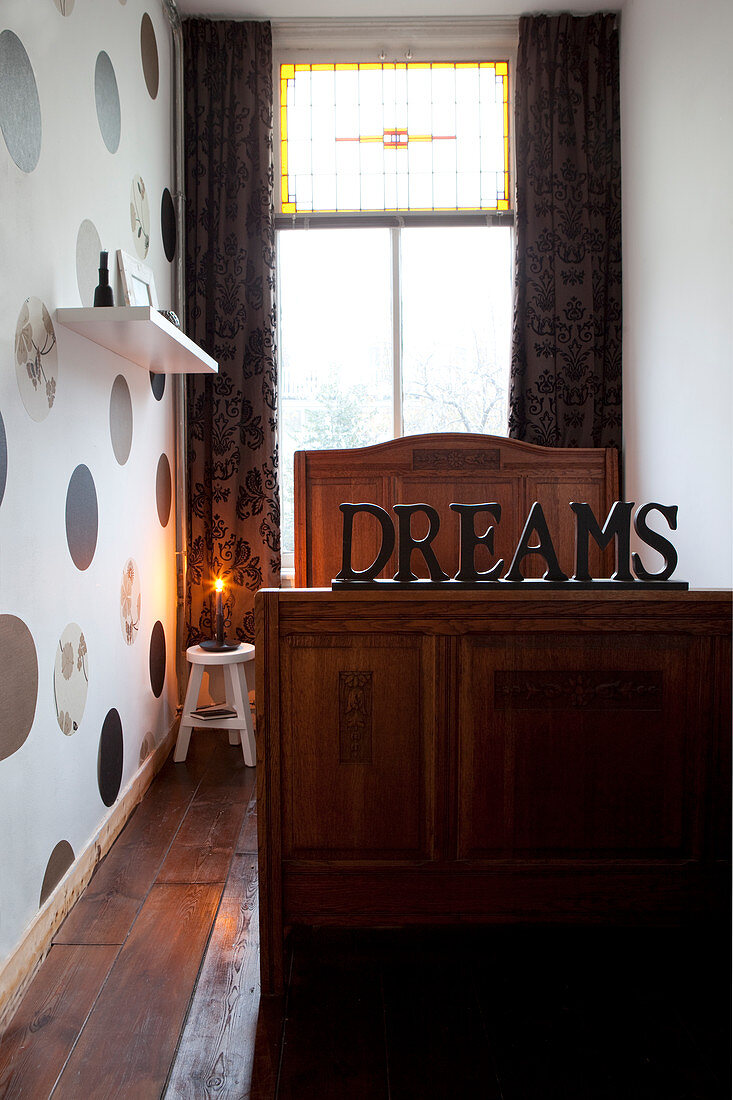 Decorative writing on an old wooden bed in a narrow room with a dotted wall paper