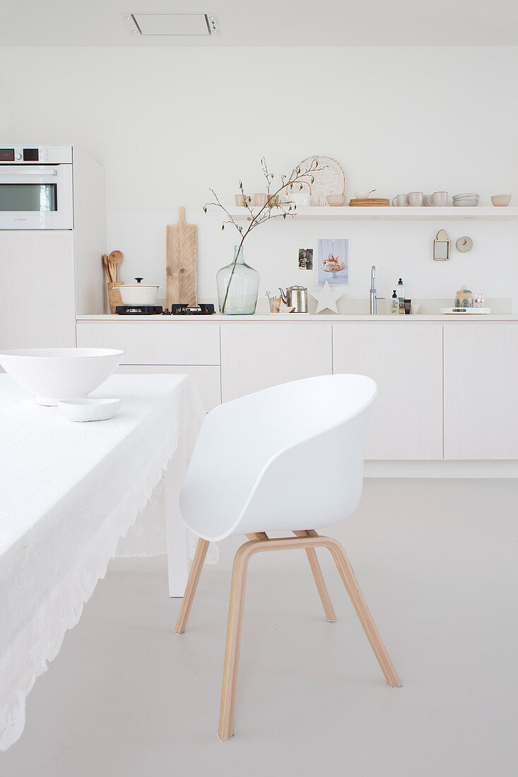 Weißer Schalenstuhl um Tisch mit weißer Tischdecke in Wohnküche mit weißer Küchenzeile