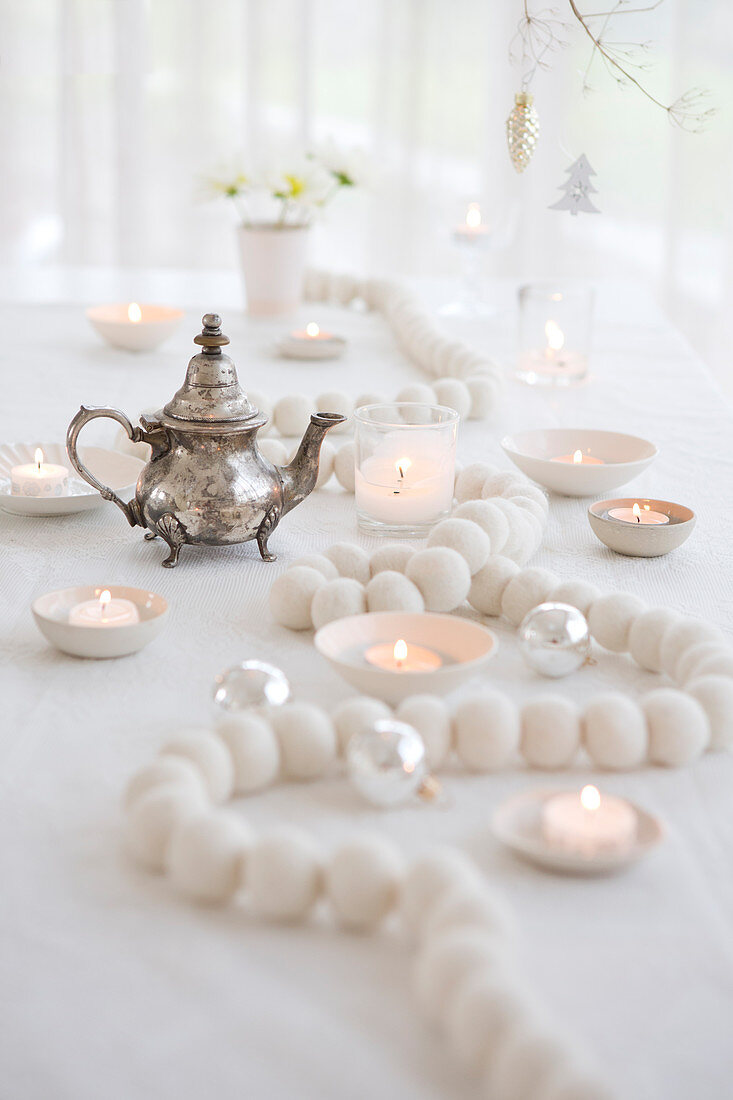 Weiße Holzperlenkette, Teelichter und silberne Teekanne auf Weihnachtstisch