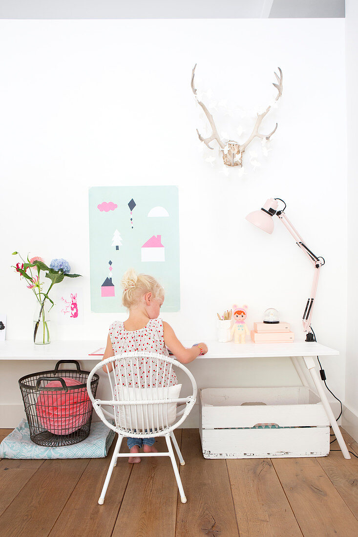 Girl seated at white desk below hunting trophy and paper decorations on wall