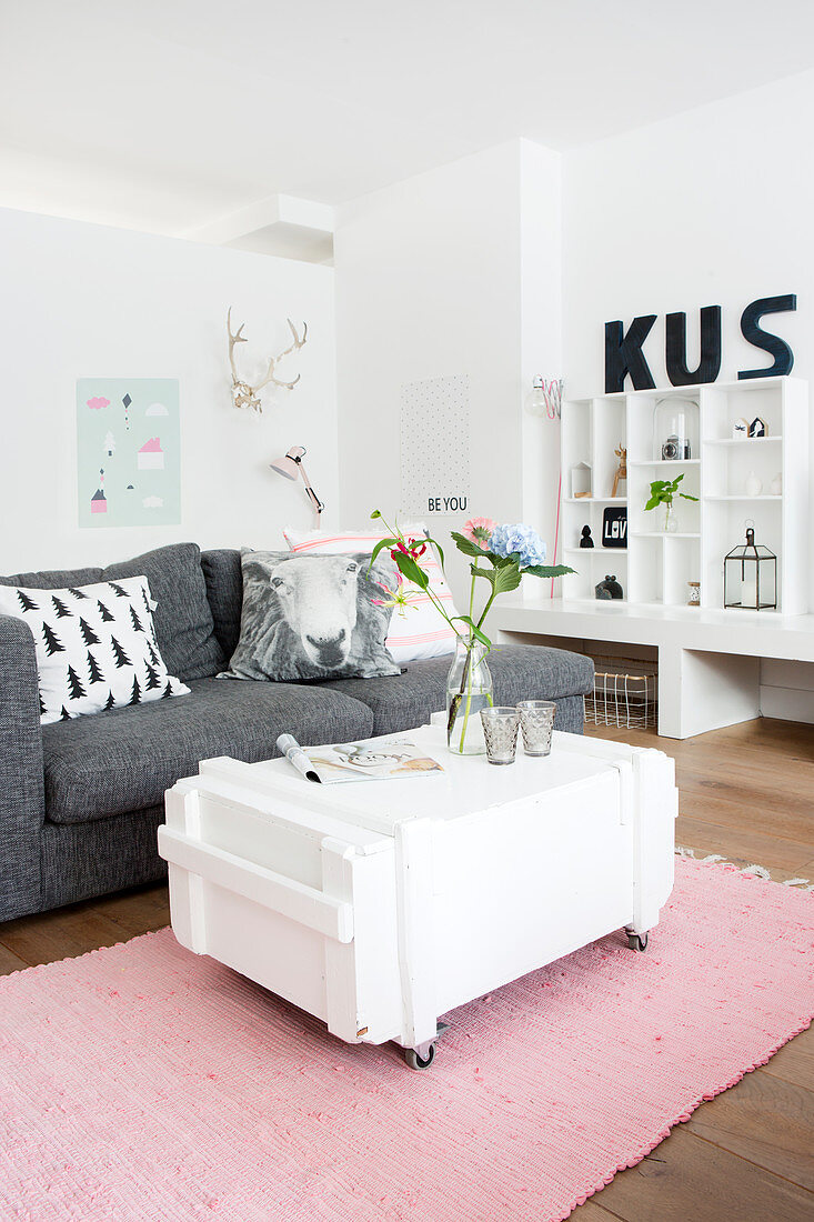 White-painted trunk on castors used as coffee table, grey sofa and shelves in living room