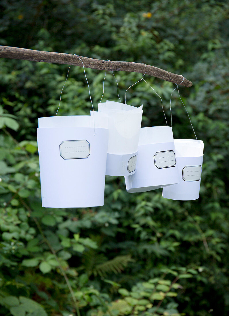 Windlichter aus Papier mit nostalgischen Etiketten an einem Stock im Garten