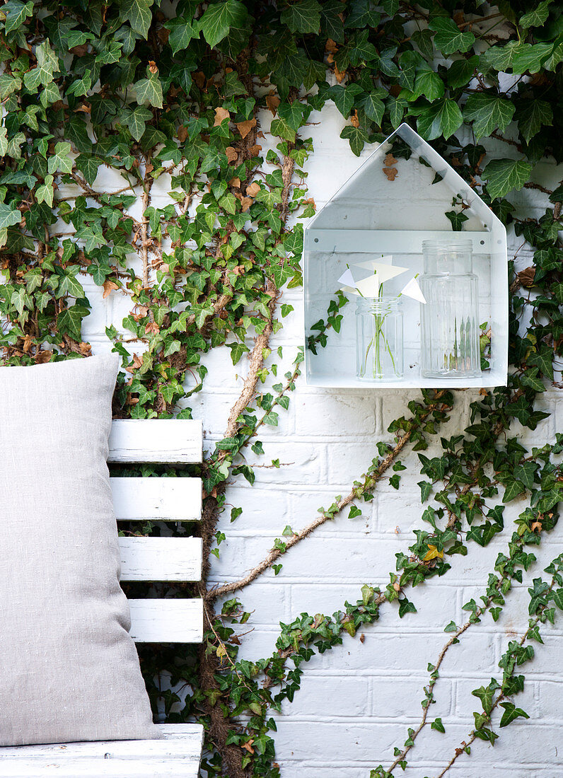 Shelf in the shape of a house on a brick wall covered with ivy