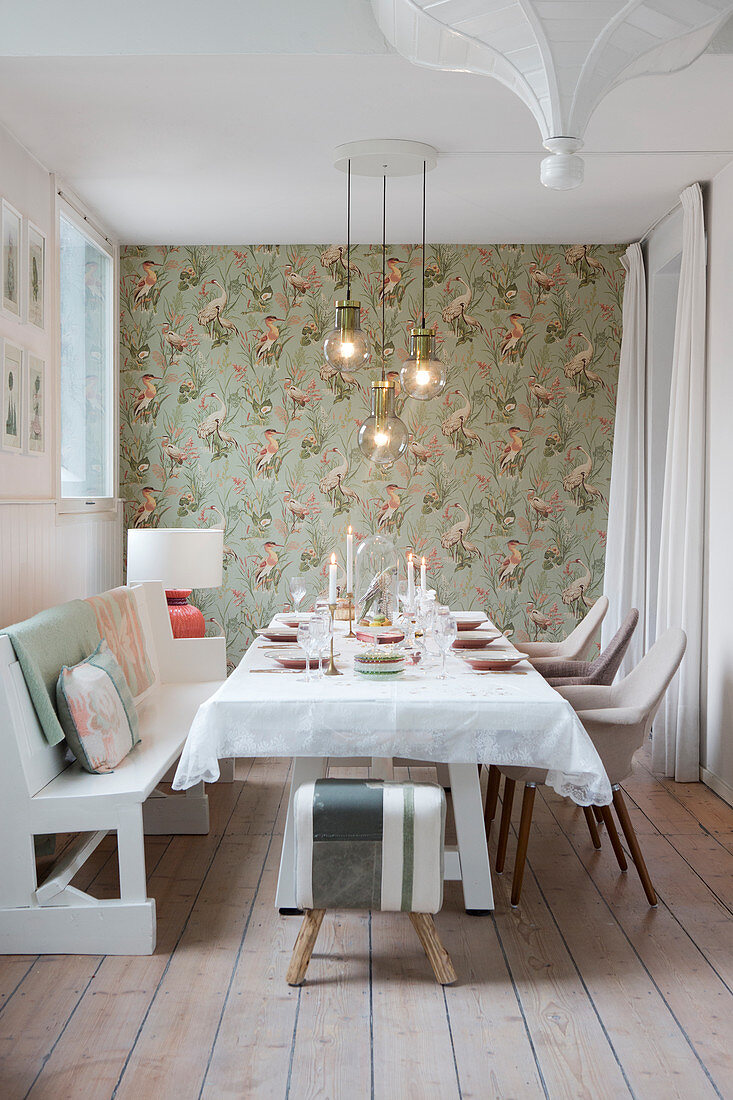 Festlich gedeckter Tisch mit weißer Bank und Stühlen im Esszimmer, an der Wand Tapete mit Vogelmotiv