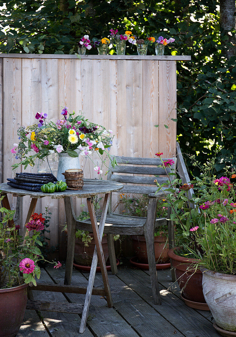 Rustikaler Sitzplatz auf der Terrasse mit Bretterwand und Sommerblumen