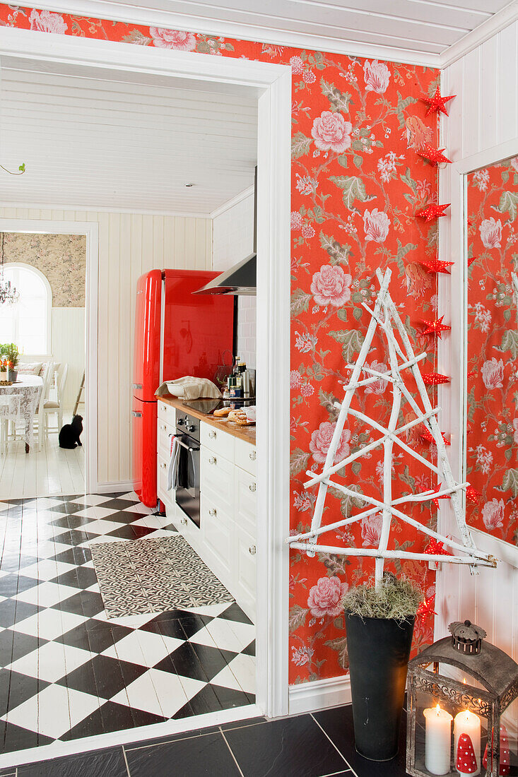 View from hallway area with red rose pattern wallpaper into kitchen with checkerboard pattern floor and red refrigerator