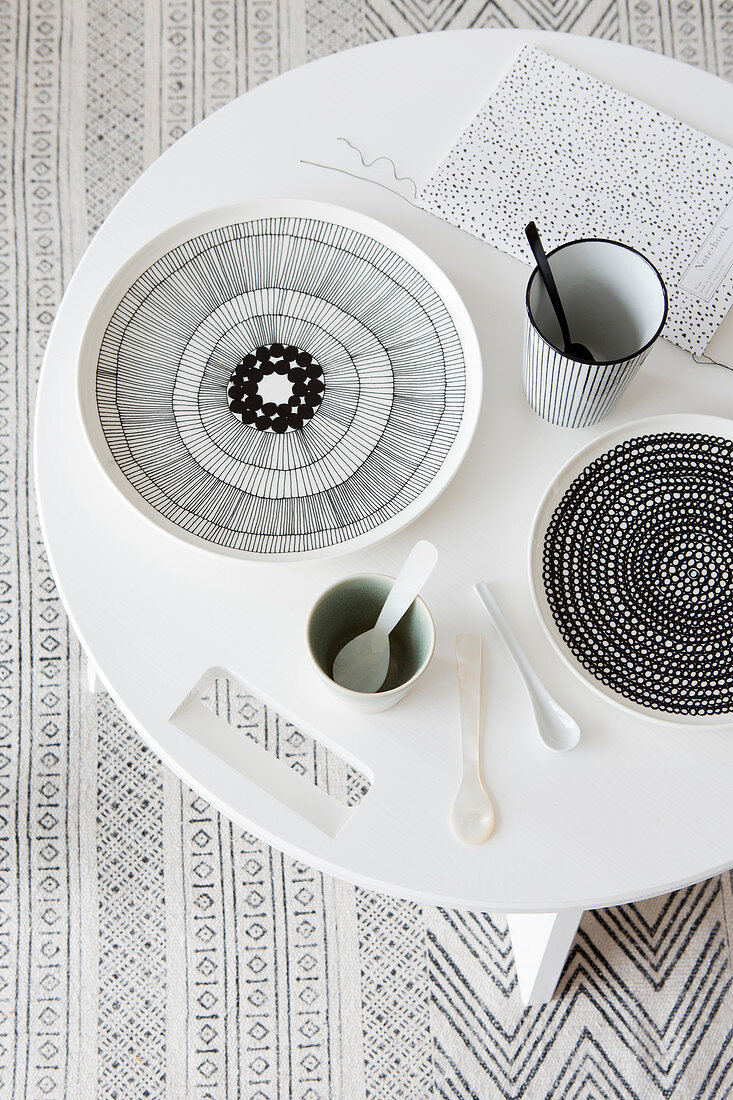 Runder Tisch mit schwarz-weißem Geschirr auf Teppich mit grafischem Muster