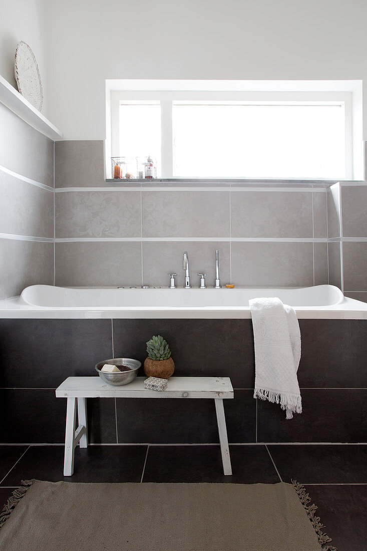 White bench in front of the bathtub under the horizontal window