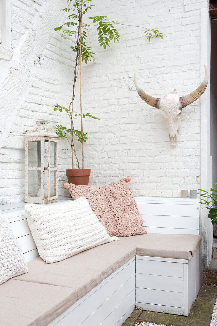 Holzbank mit Kissen und Geweih auf Terrasse mit weiß getünchter Ziegelwand