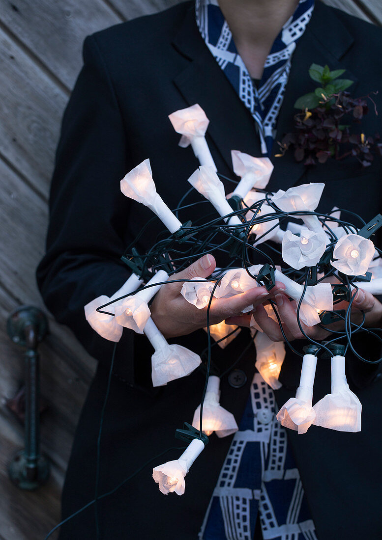 Hände halten Lichterkette mit selbstgemachten Papierblüten