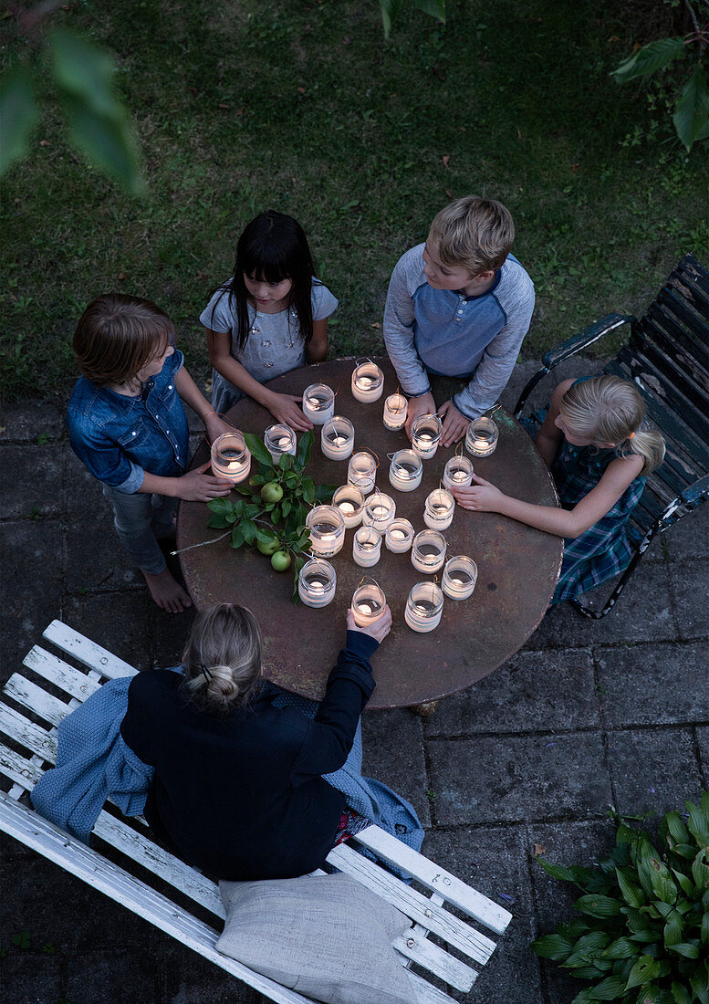 Kinder um runden Gartentisch mit selbstgemachten Windlichtern