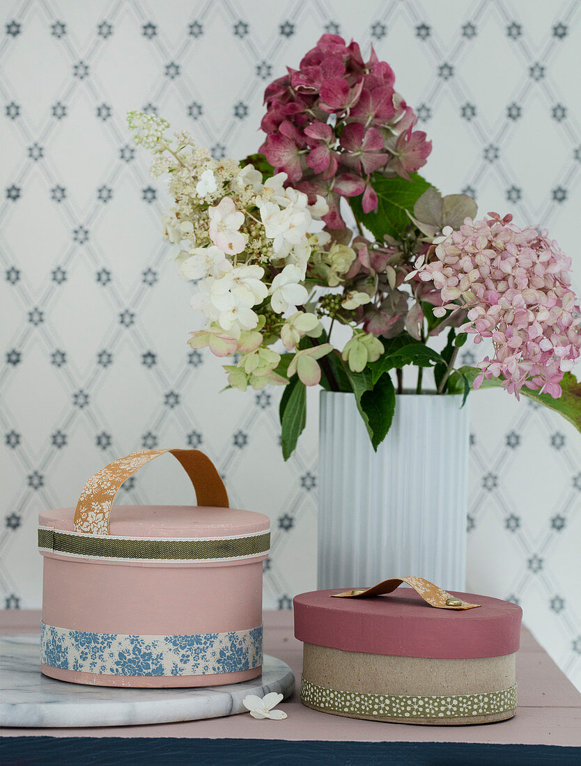 Mit Stoffbändern beklebte Schachteln und Vase mit verschiedenen Hortensien