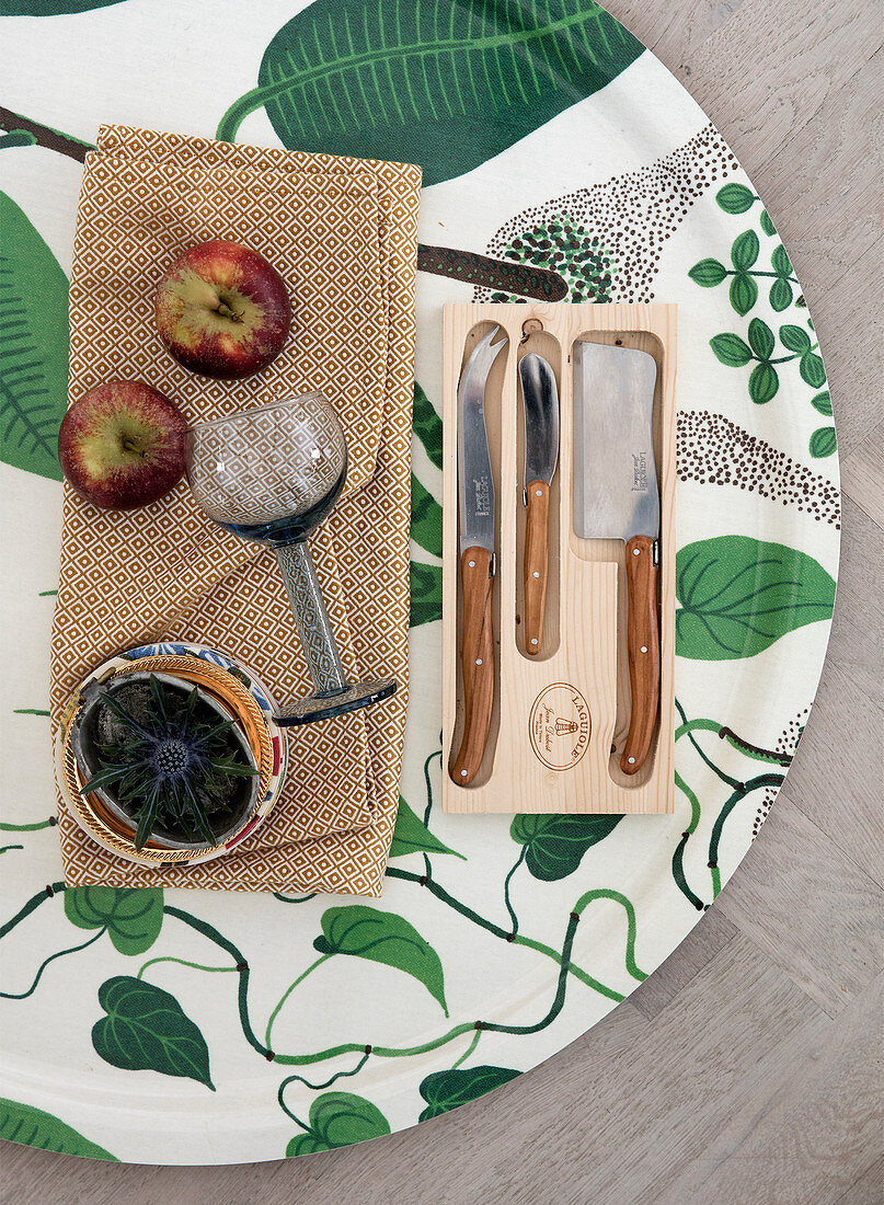 Messer, Äpfel, Diestel und Weinglas auf einem Tablett mit floralem Muster