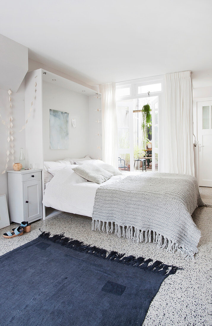 A blue rug in front of double bed with grey knitted blanket