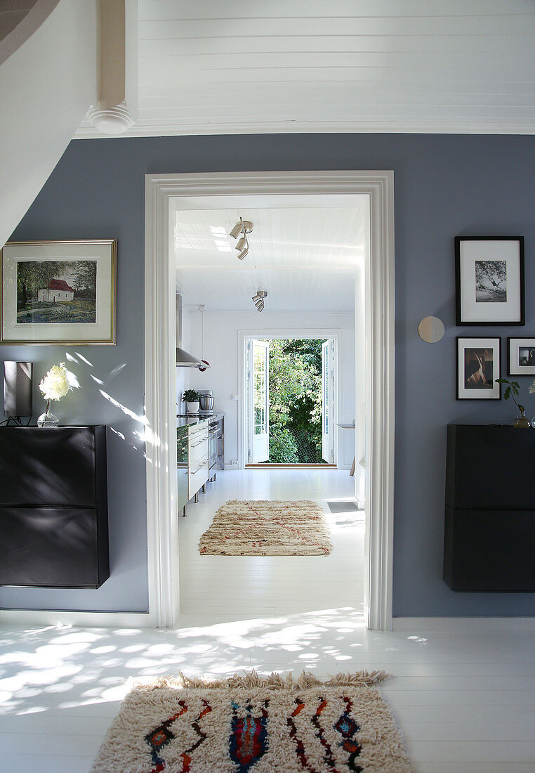 A hallway with a grey-blue wall and a view into a kitchen