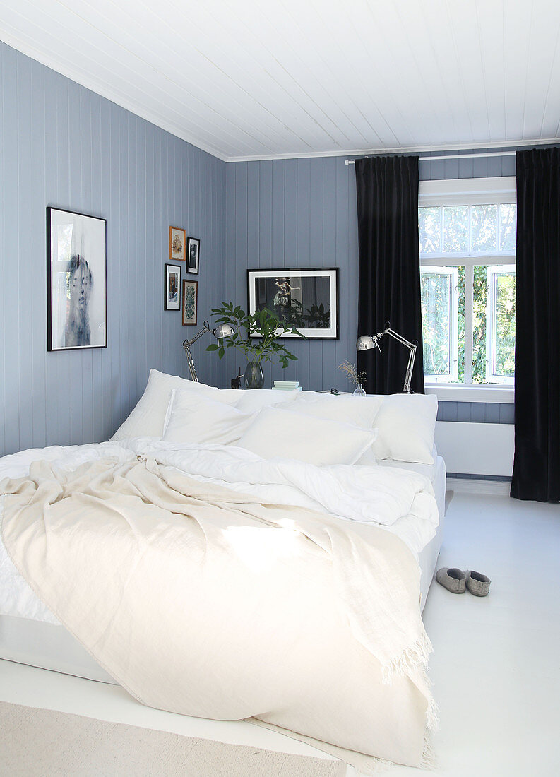 Doppelbett und schwarze Vorhänge in blau-grauem Schlafzimmer