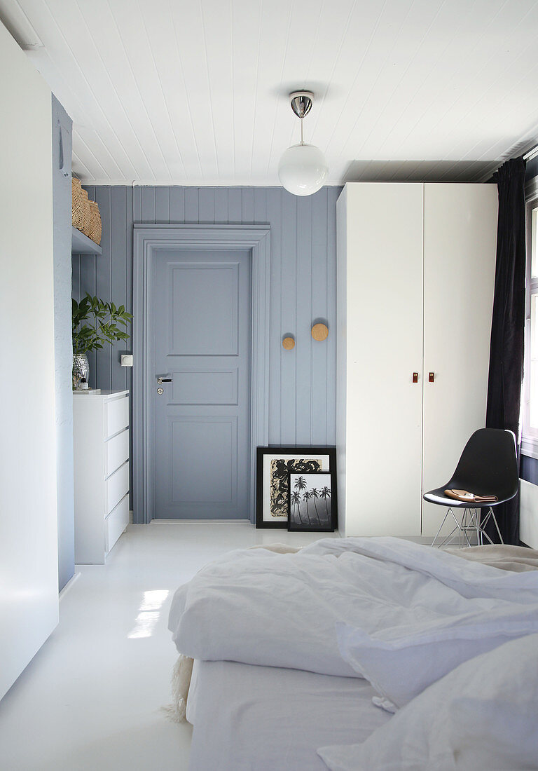 A double bed, a black chair, a white wardrobe and a chest of drawers in a blue-grey bedroom