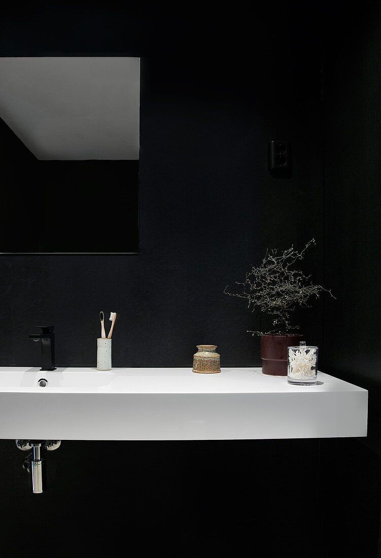 Weißer Waschtisch vor schwarzer Wand im Badezimmer