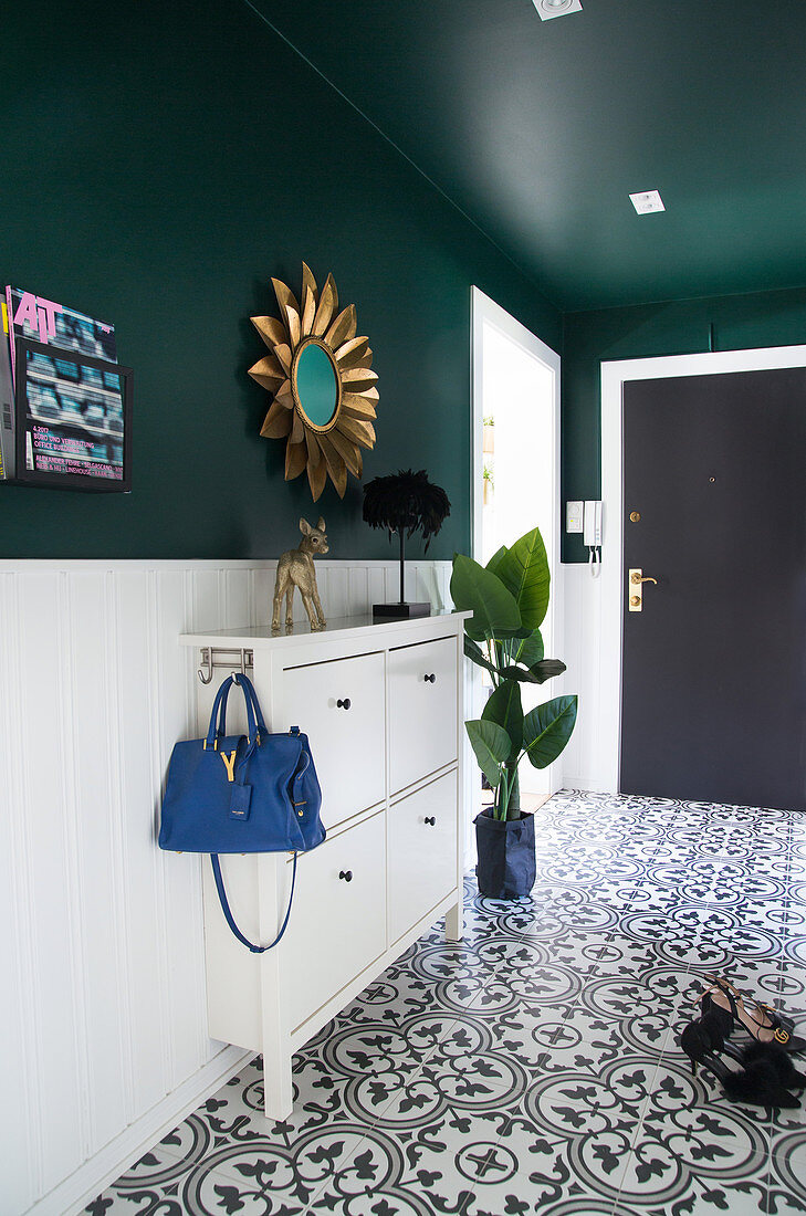 White shoe cabinet and sun mirror in the hallway with green wall and tiled floor