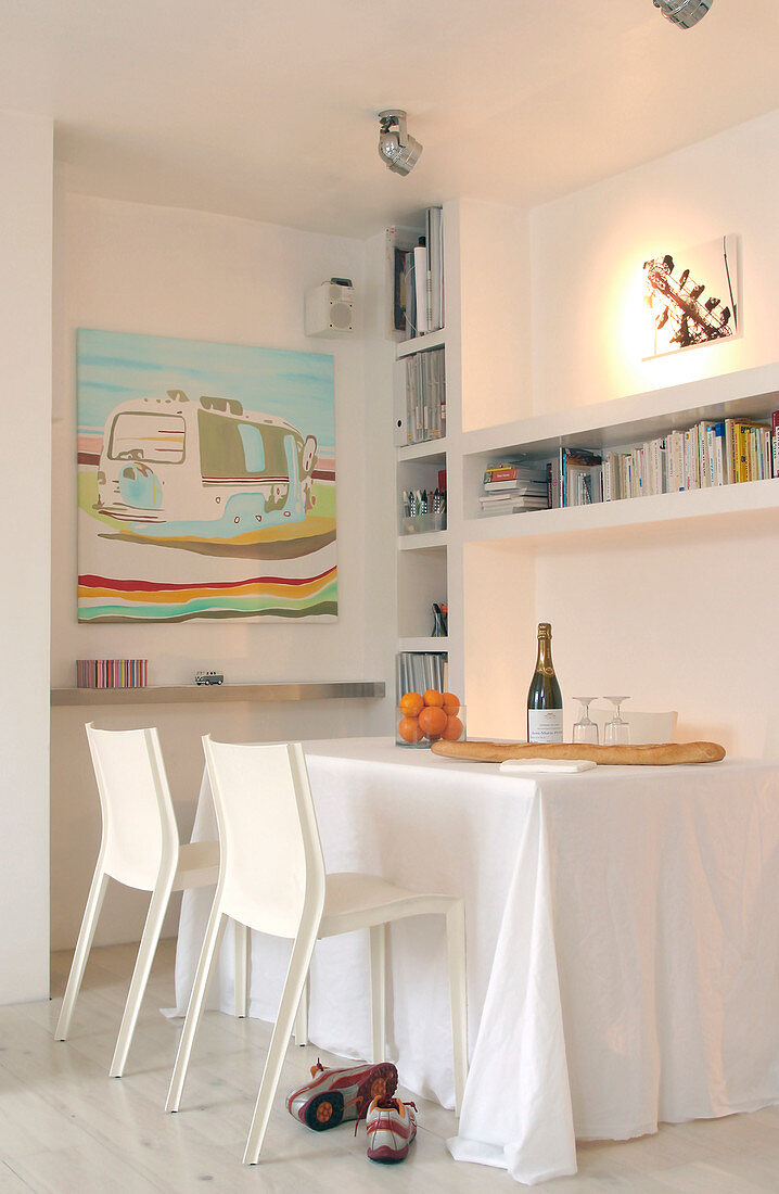White chairs in front of a table with a tablecloth under built-in shelves