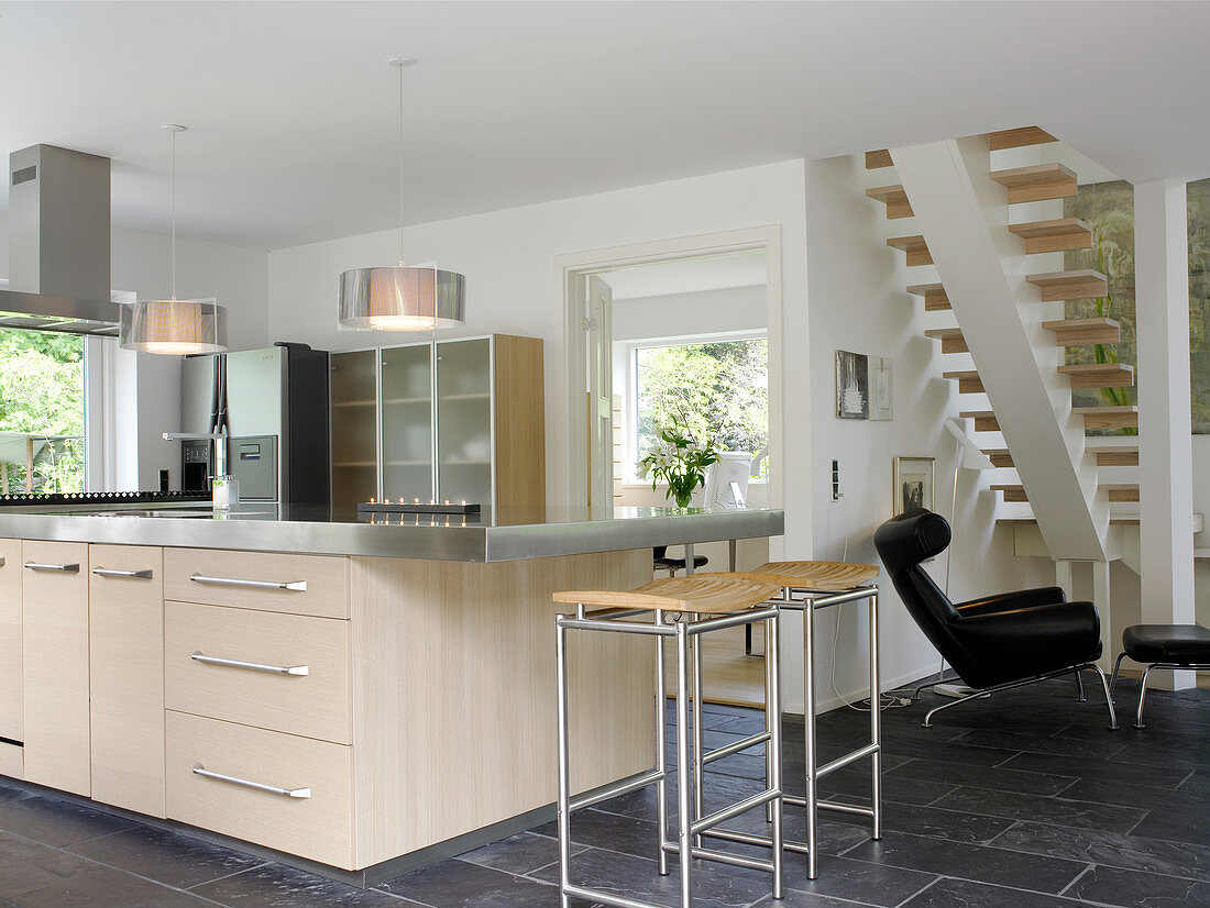 Kücheninsel mit hellem Front und Edelstahl-Arbeitsplatte, Barhocker und Designerstuhl in offener Küche