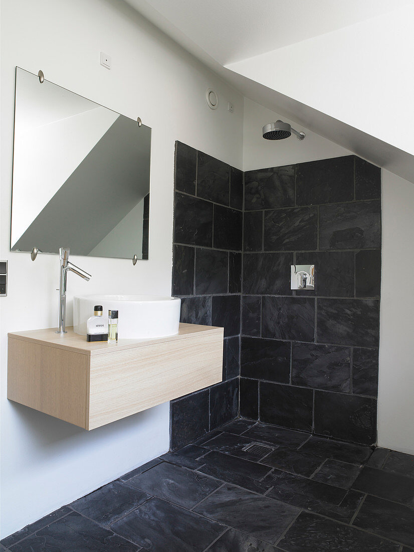 Simple vanity under the mirror in a white bathroom with anthracite-colored tiles