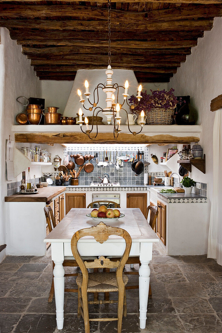 A chandelier above the dining table in a rustic open kitchen - dining room with a natural stone floor