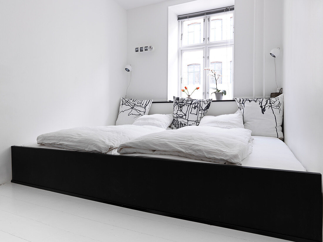 A wide family bed across the entire width of the room in a white bedroom