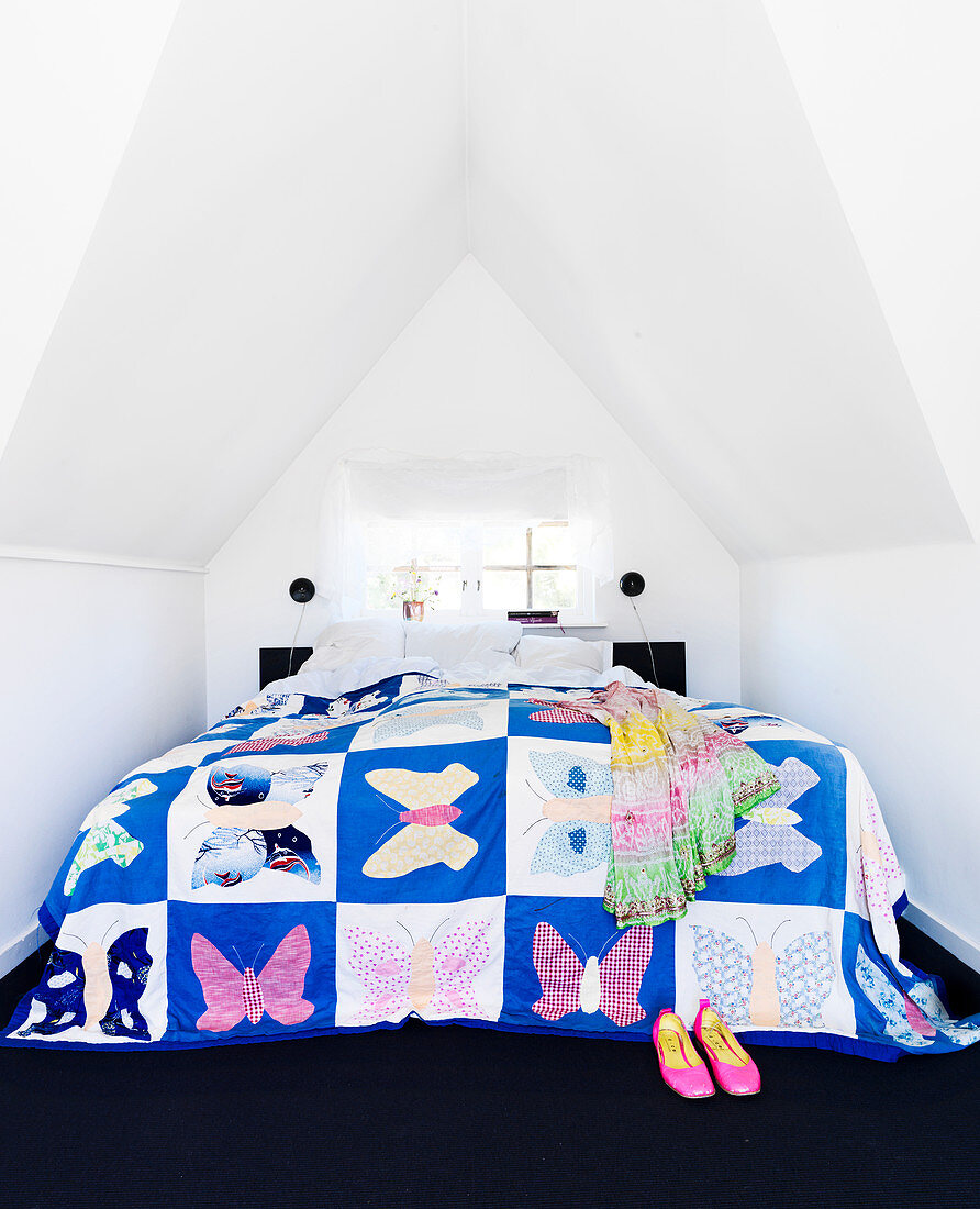 Patchwork quilt with butterflies on the bed under the eaves of the ceiling