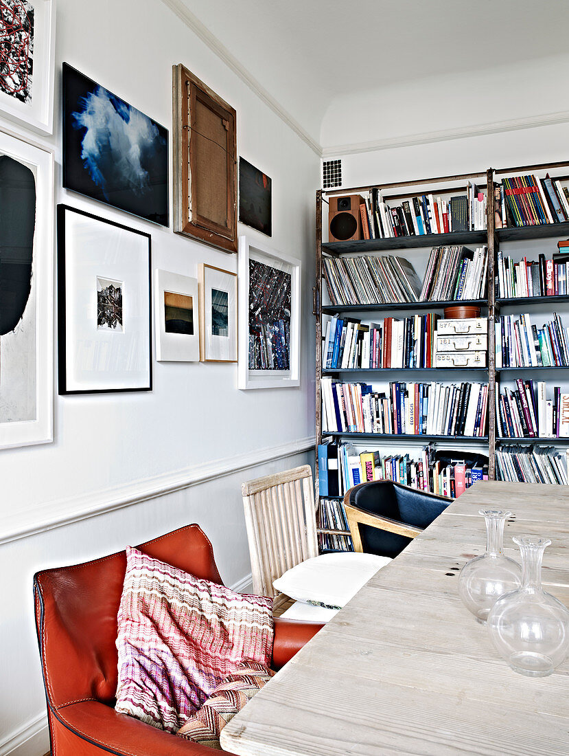 Verschiedene Stühle am Esstisch vorm Bücherregal und der Bilderwand