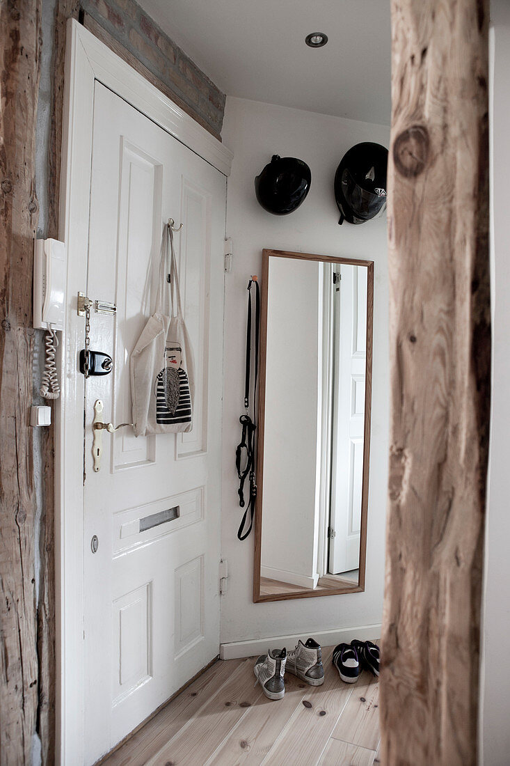 White entrance door with various locks and wall mirror in the entrance area with rustic wooden supports