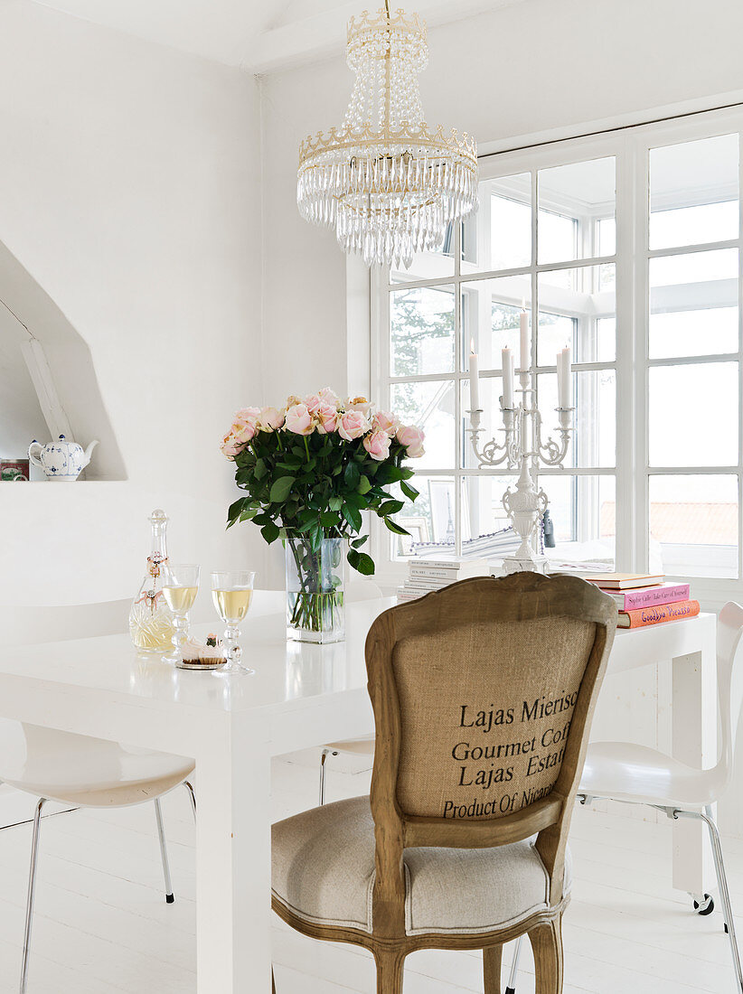 Barockstuhl am weißen Tisch mit Rosenstrauß unterm Kronleuchter