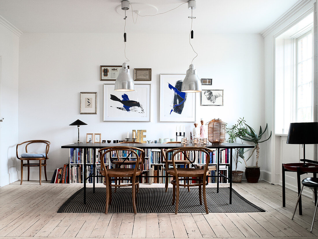 Schwarzer Esstisch mit Thonetstühlen vor halbhohem Bücherregal und Lithografien an weißer Wand