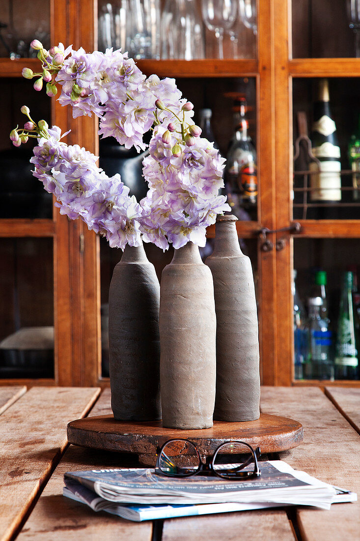 Drei Vasen mit Blumen, im Hintergrund Geschirrschrank