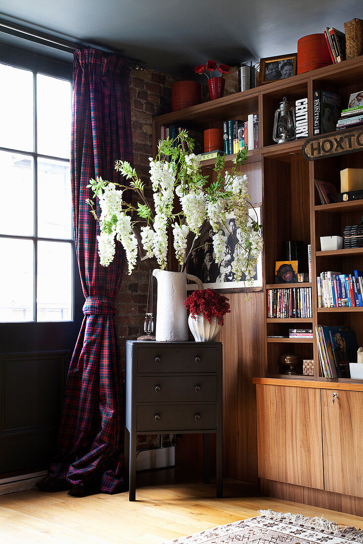 Vase mit Blütenzweigen auf Schubladenschränkchen vor Fenster