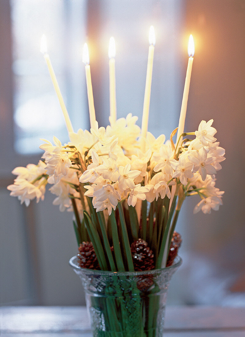 Weiße Blumen mit Zapfen und Kerzen in Kristallvase