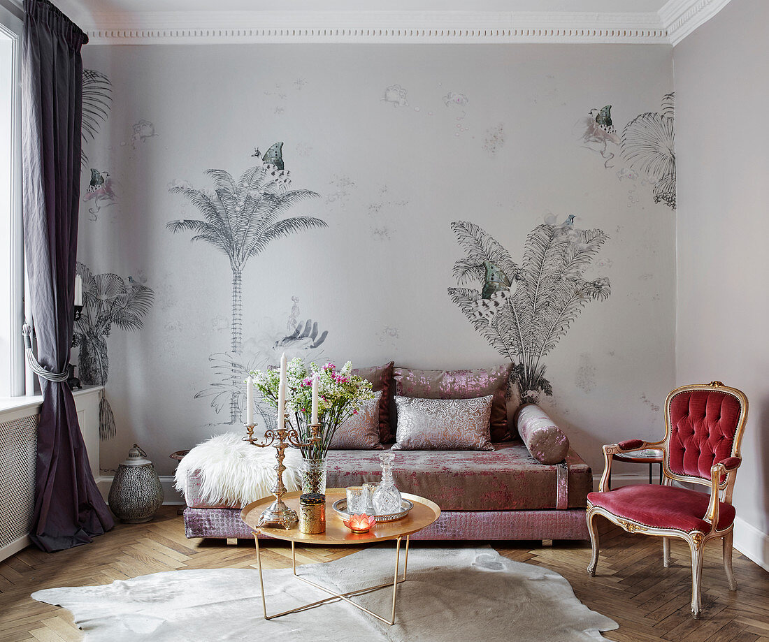 Elegantes Sofa vor Tapete mit Palmenmotiv, Couchtisch und antiker Stuhl im Wohnzimmer